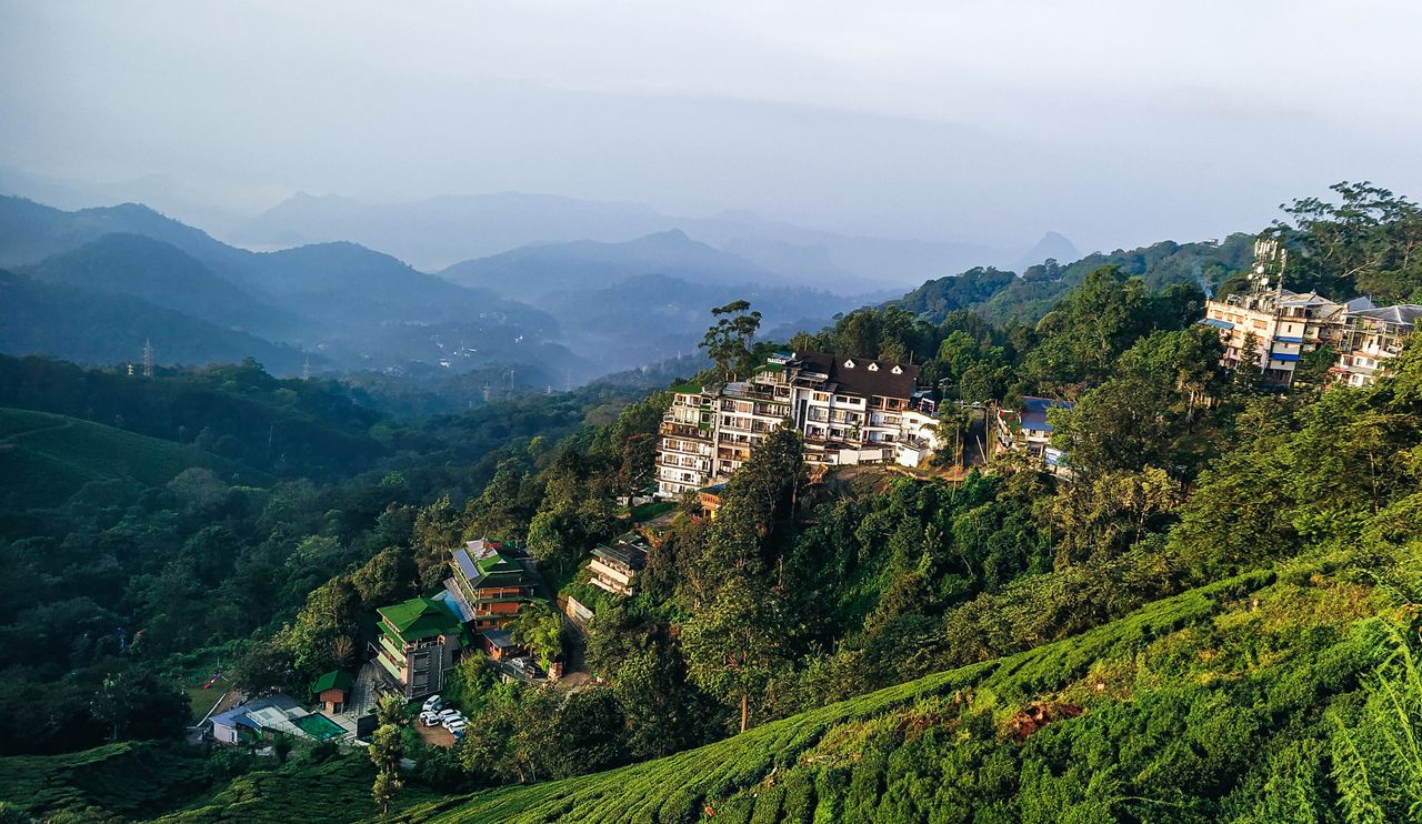 Majestic mountain view with buildings nestled among lush greenery under a clear sky.