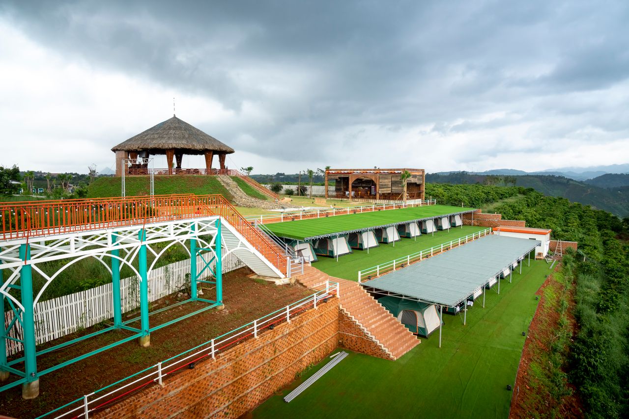 Hotel with staircase and covered terraces near traditional wooden structures located amidst dense forest with green trees in tropical country